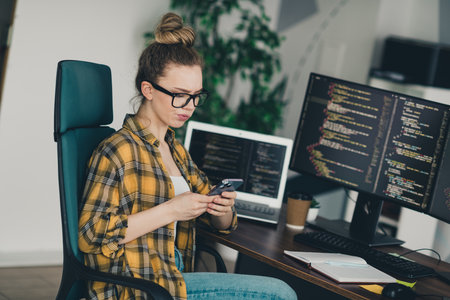 Female computer programmer coding in a stylish office, focused on developing software and analyzing code on a smartphoneの写真素材
