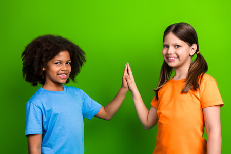 Two schoolgirls giving a joyful high-five on a vibrant green background showcasing positivity and cheerful friendshipの写真素材