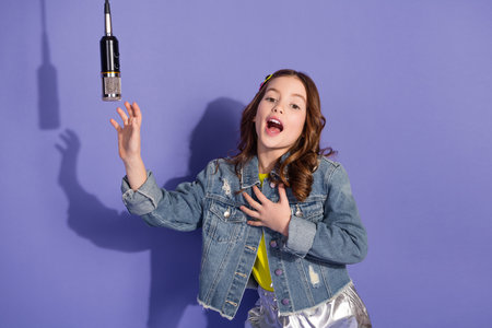 Young girl singing with passion in a stylish denim jacket against a violet background, expressing joy and confidenceの写真素材