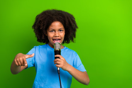 Young girl singing into microphone with enthusiastic expression against a vibrant green background wearing casual attireの写真素材