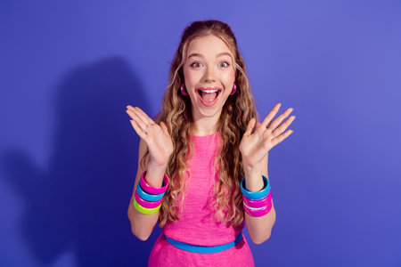 Excited young woman in vibrant fashion posing with cheerful expression against a purple background,...