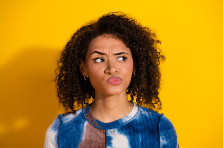 Close-up of a thoughtful young female wearing a casual patterned shirt against a vibrant yellow backgroundの写真素材