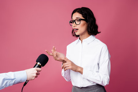 Charming brunette businesswoman speaking during an interview in a modern outfit against a vibrant pink backgroundの写真素材