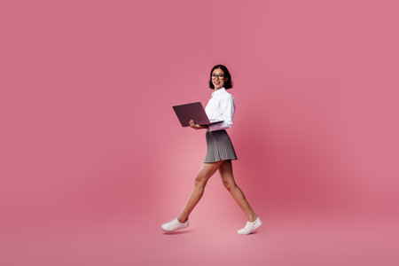 Charming Businesswoman in a Stylish Outfit on a Pink Background Holding a Laptop and Smiling Brightlyの写真素材