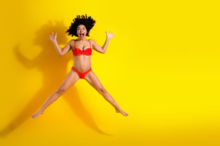 Joyful woman in a red bikini jumping against a vibrant yellow background with a playful expression and energetic vibeの写真素材