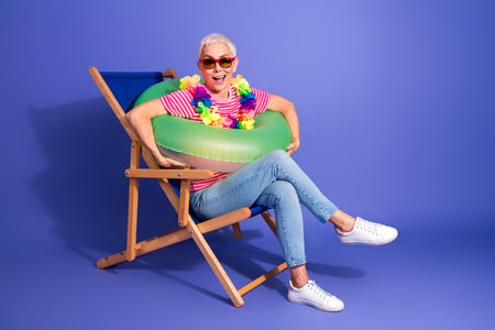 Smiling elderly woman with inflatable float on chair, enjoying leisure on a colorful backgroundの写真素材