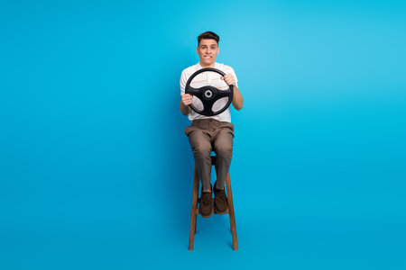 Young man holding a steering wheel with a humorous expression against a bright blue backgroundの写真素材