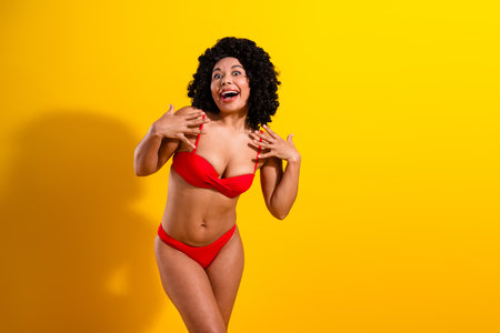 Joyful woman posing in red swimwear against yellow backdrop, expressing happiness and body positivity with vibrant charmの写真素材