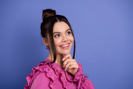 Portrait of a cheerful young woman in stylish ruffled pink attire against a vibrant purple background, exuding charmの写真素材