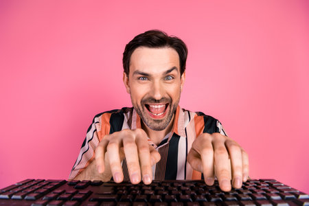 Excited young man with striped shirt typing on keyboard against pink background showcasing enthusiasm and humorの写真素材