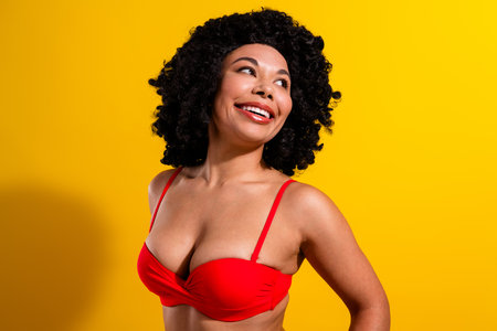 Confident woman in red bikini enjoying vibrant yellow background and embracing her beauty with an elegant smileの写真素材