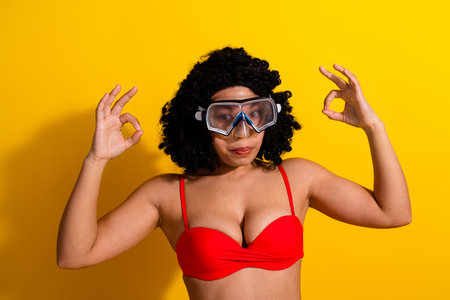 Beautiful woman wearing swim goggles posing confidently against a vibrant yellow background, expressing joy and summer vibesの写真素材