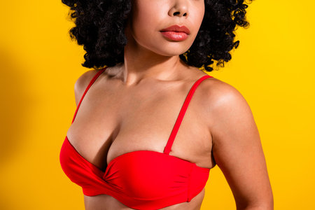 Attractive young woman in red bikini top standing confidently against a vibrant yellow background, showcasing beauty and styleの写真素材