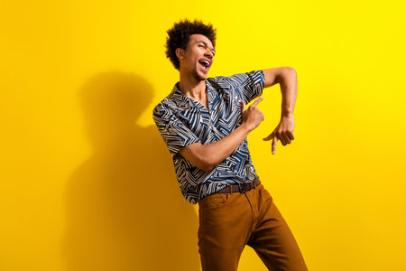 Energetic young man in stylish outfit gesturing enthusiastically against vibrant yellow background...