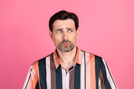 Handsome Man in a Striped Shirt Looking Thoughtful Against a Pink Background Depicting Casual and...