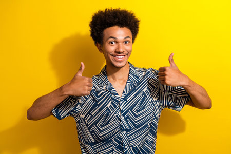 Cheerful man in stylish attire giving thumbs up against vibrant yellow background, expressing...