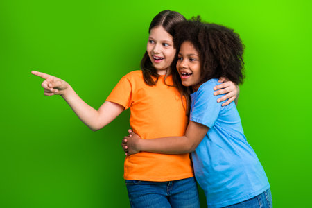 Two cheerful schoolgirls pointing at something exciting while embracing each other, showcasing joy and teamworkの写真素材