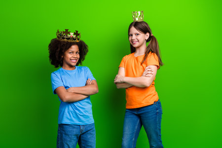 Two smiling girls with crowns posing confidently against a vibrant green background showcasing individuality and friendshipの写真素材