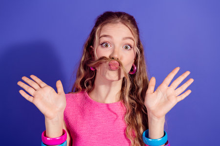 Playful young woman with long blonde hair making funny expressions against a vibrant purple...