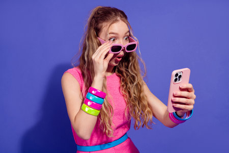 Youthful woman in trendy pink outfit enjoys smartphone interaction with excitement against a vibrant...