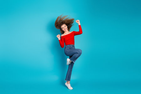 Young woman jumping joyfully in a casual outfit on a vibrant blue background showcasing cheerful energy and trendy styleの写真素材