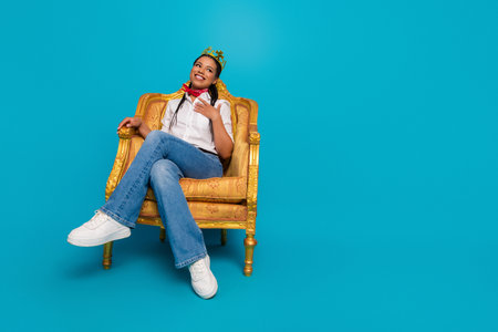 Young woman with charming smile sitting on an ornate chair in a casual outfit, blue background, stylish and elegantの写真素材