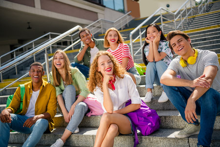 Young friends sitting on outdoor steps enjoying a sunny day and bonding in a lively urban settingの写真素材