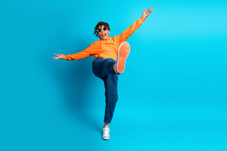 Energetic young boy in orange hoodie makes dynamic pose against bright blue background, showing playful energy and youthful styleの写真素材