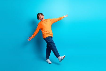 Cheerful boy in orange hoodie posing playfully on bright blue background, illustrating youthful energy and vibrant fashionの写真素材