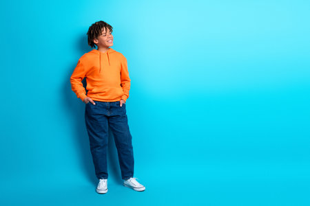 Cheerful young boy in bright orange hoodie posing confidently against a vibrant blue background, exuding fun and stylish vibesの写真素材