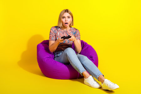 Excited young woman plays video games on a gaming chair against a vibrant yellow background, showcasing fun and leisureの写真素材