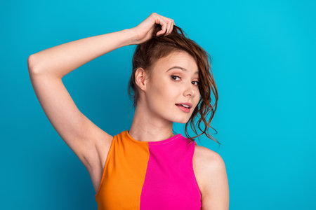 Portrait of a young woman in a vibrant outfit posing with a playful expression against a bold blue...