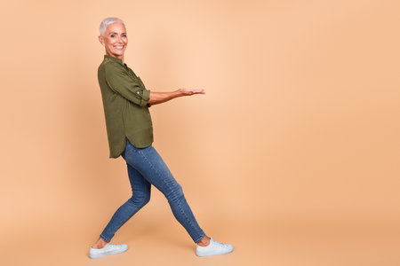 Smiling mature woman presenting something with a cheerful gesture, stylish casual outfit, beige backgroundの写真素材