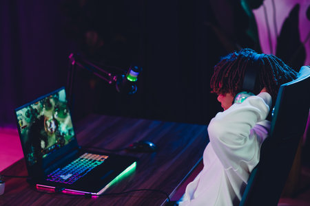 Young gamer livestreaming gameplay from a neon-lit desk setup, using a laptop and headphonesの写真素材