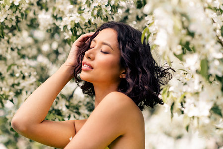Young woman posing gracefully among blooming white flowers during daylight, embodying springtime beautyの写真素材