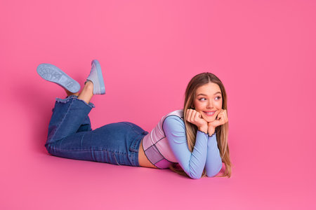 Cute young woman lying on pink background with casual trendy outfit and cheerful attitudeの写真素材