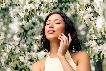 Gorgeous woman enjoying a sunny spring day amidst blooming trees, exuding beauty and elegance with a...