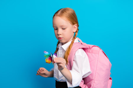 Adorable schoolgirl with red hair holding a butterfly, wearing a pink backpack, standing against a...