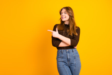 Young cheerful woman in trendy casual clothing standing against a vibrant yellow background and looking optimisticの写真素材