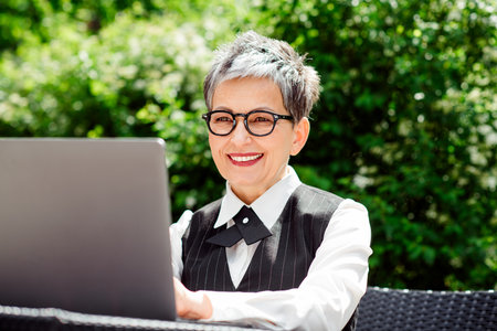 Confident businesswoman working outdoors with a notebook computer during a sunny summer dayの写真素材