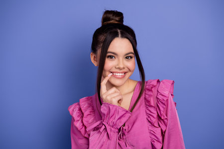 Charming brunette woman in pink ruffled dress posing with a captivating smile against a vibrant...