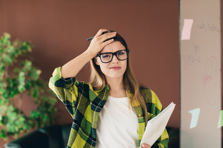 Young female entrepreneur reflects at whiteboard during brainstorming with casual style in coworking...
