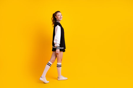 Confident young woman in a trendy varsity jacket posing against a cheerful yellow background exuding style and charmの写真素材