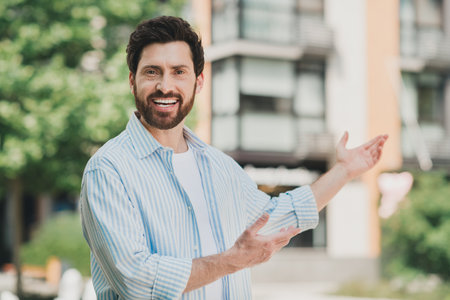 Smiling handsome man standing outdoor in casual attire with open arms on a sunny day in an urban environmentの写真素材