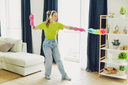 Young woman cleaning a cozy living room interior while listening to music and enjoying springtime activities.の写真素材