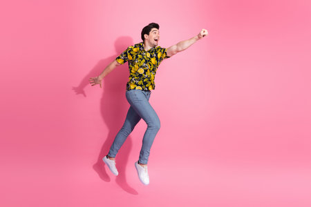 Young man posing energetically against a pink backdrop in a stylish tropical print shirt and jeans