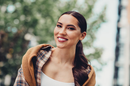 Smiling young brunette woman enjoying a casual walk outdoors during a pleasant urban spring dayの写真素材