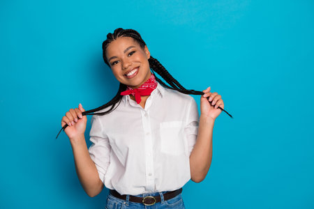 Young woman with braids and red scarf posing against blue background in a white shirt while smiling...