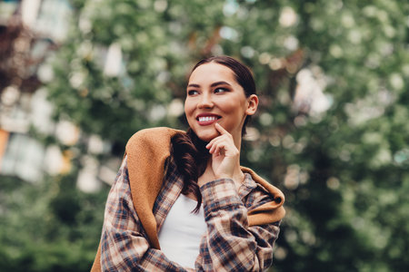 Cheerful young woman enjoying a beautiful day outdoors in casual attire with a stylish scarf and relaxed demeanorの写真素材