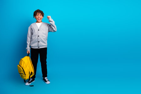 Enthusiastic schoolboy with a yellow backpack and bright expression on blue background - education and learning conceptの写真素材